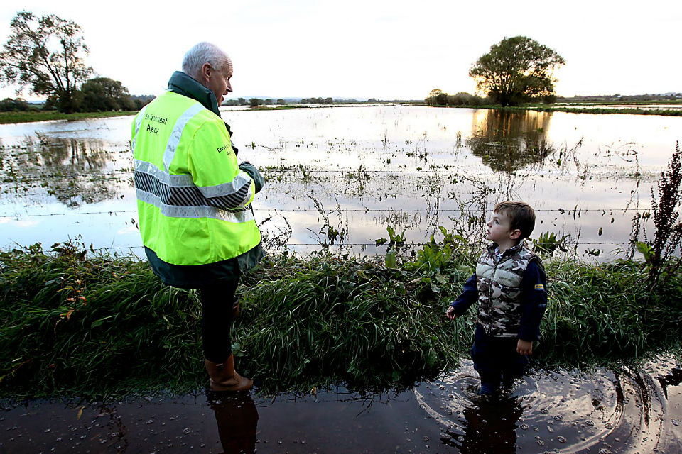 Man in high-vis jacket on flooded path with small boy