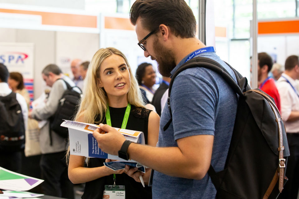 A woman and a man in conversation at the Government Counter Fraud Profession stand at Civil Service Live 2018