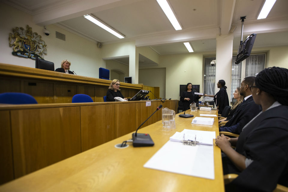 Courtroom proceedings in progress with video screens and computers in use by court officials