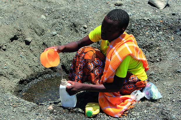 A woman scoops water from a nearly dry riverbed in northern Kenya