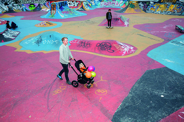 Man pushing a pushchair with a baby inside holding multi-coloured balloons